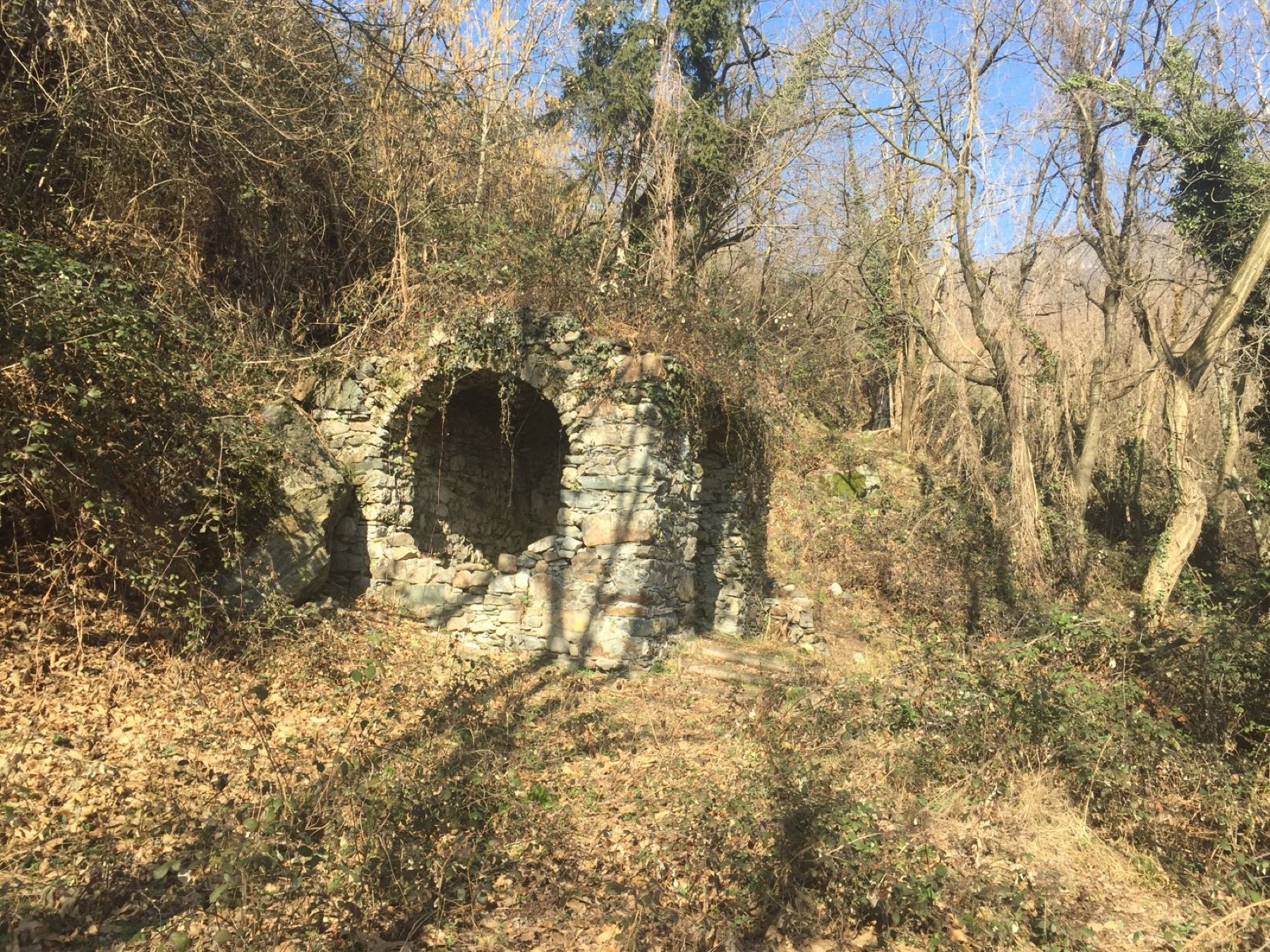 Il rudere della cappella di San Rocco in inverno, con le mura in pietra avvolte dai rovi spogli e dalla neve, prima del restauro